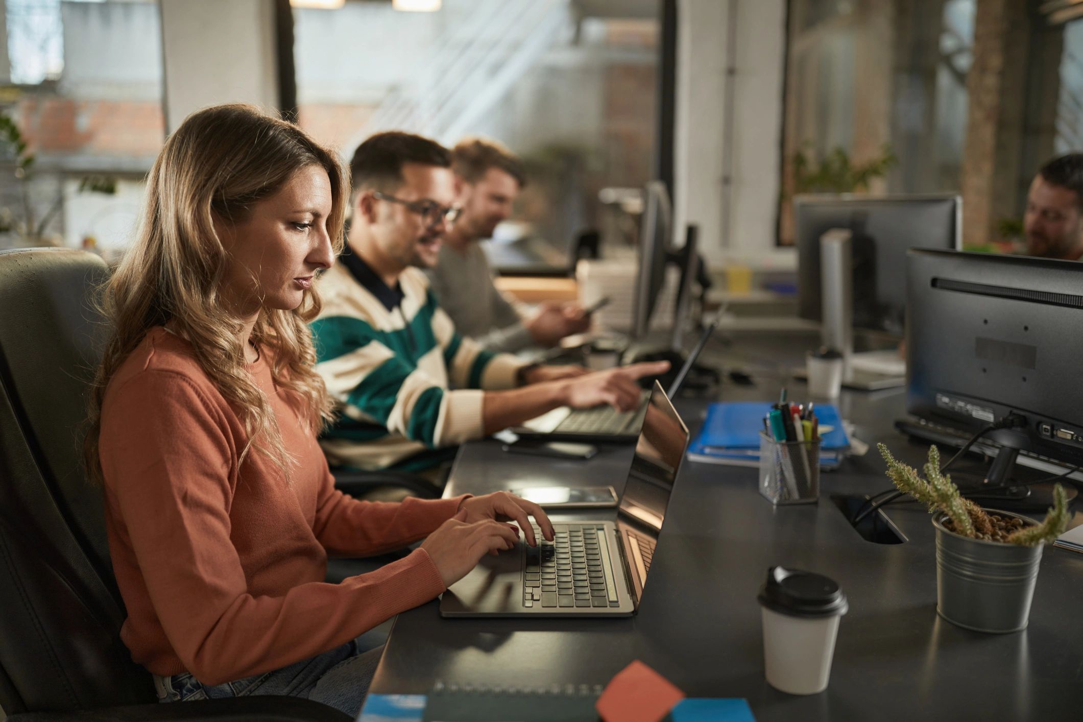 IT professional working on a laptop with colleagues in the background