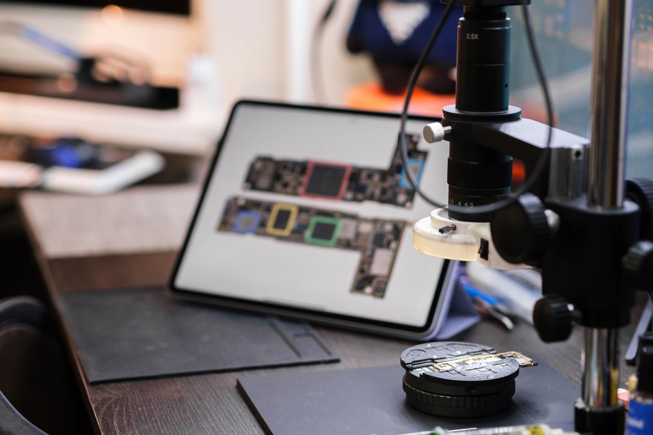 Electronics repair workbench with tools and circuit board under magnifier